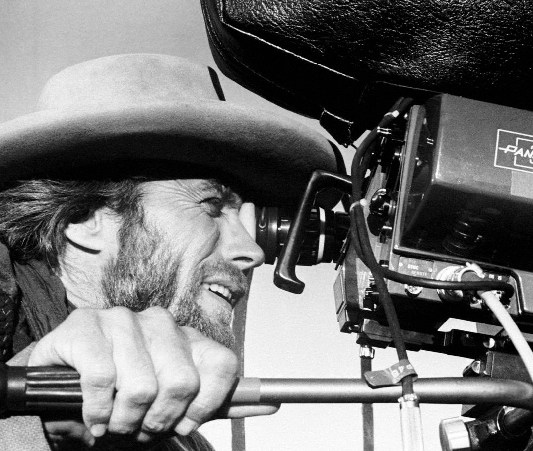 Clint Eastwood, sonriendo bajo un sombrero vaquero, mirando por el visor de una cámara Panavision