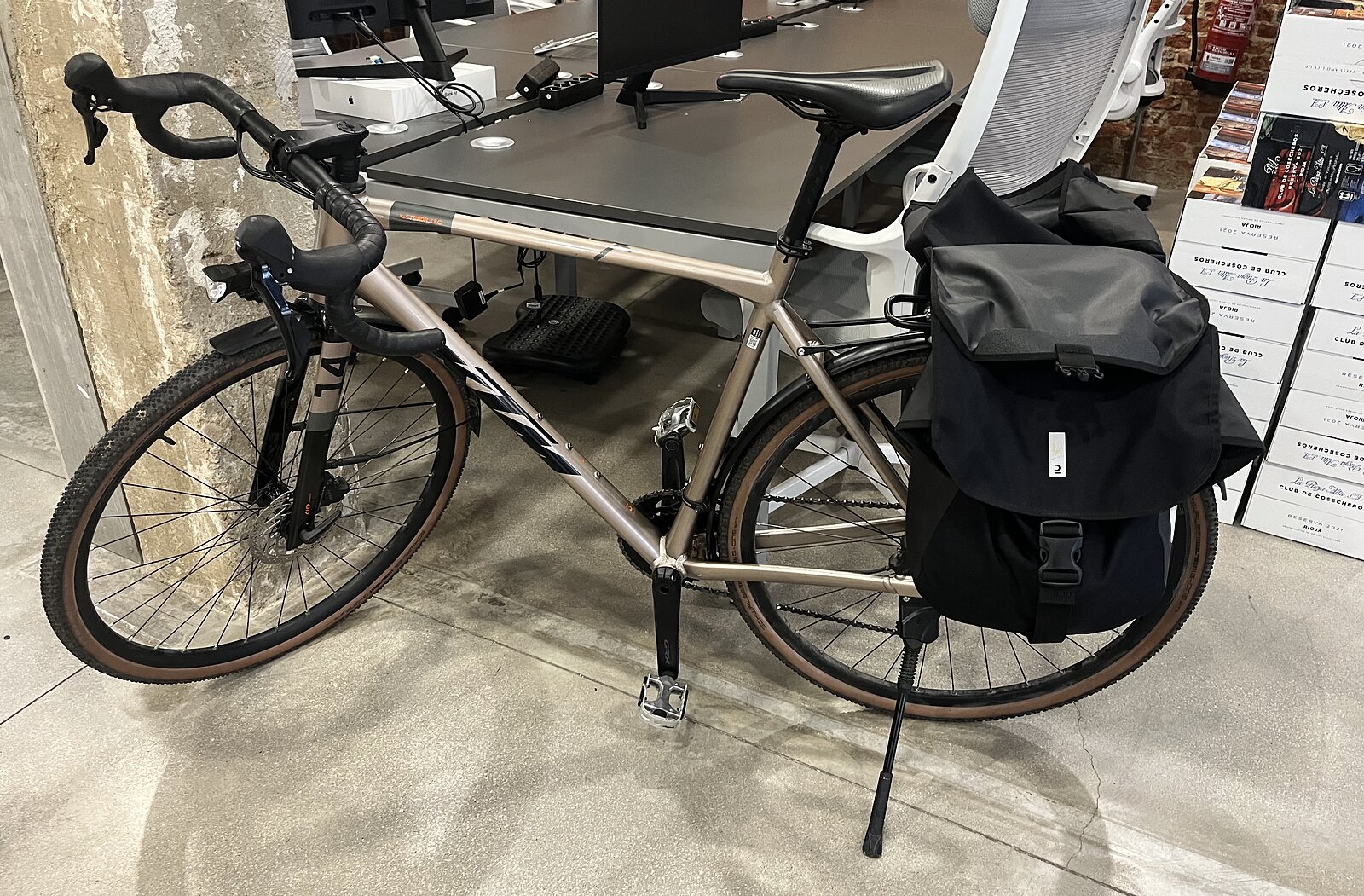 A gravel bike with black panniers parked next to the desks at the Dcycle office